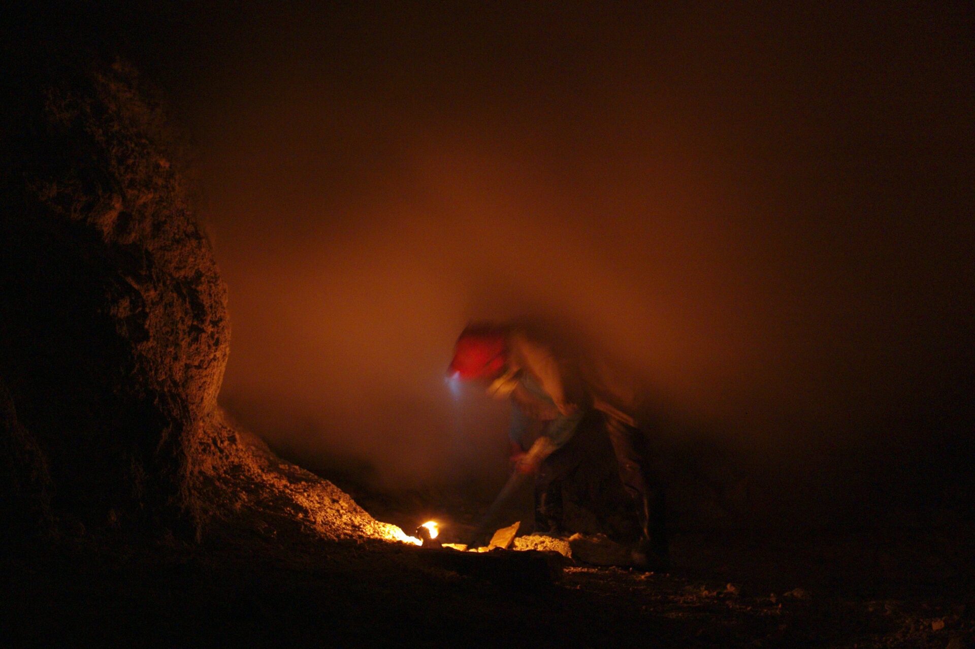 Using a long crow bar, miners tear raw sulfur from the Ijen volcano as steam blows over them