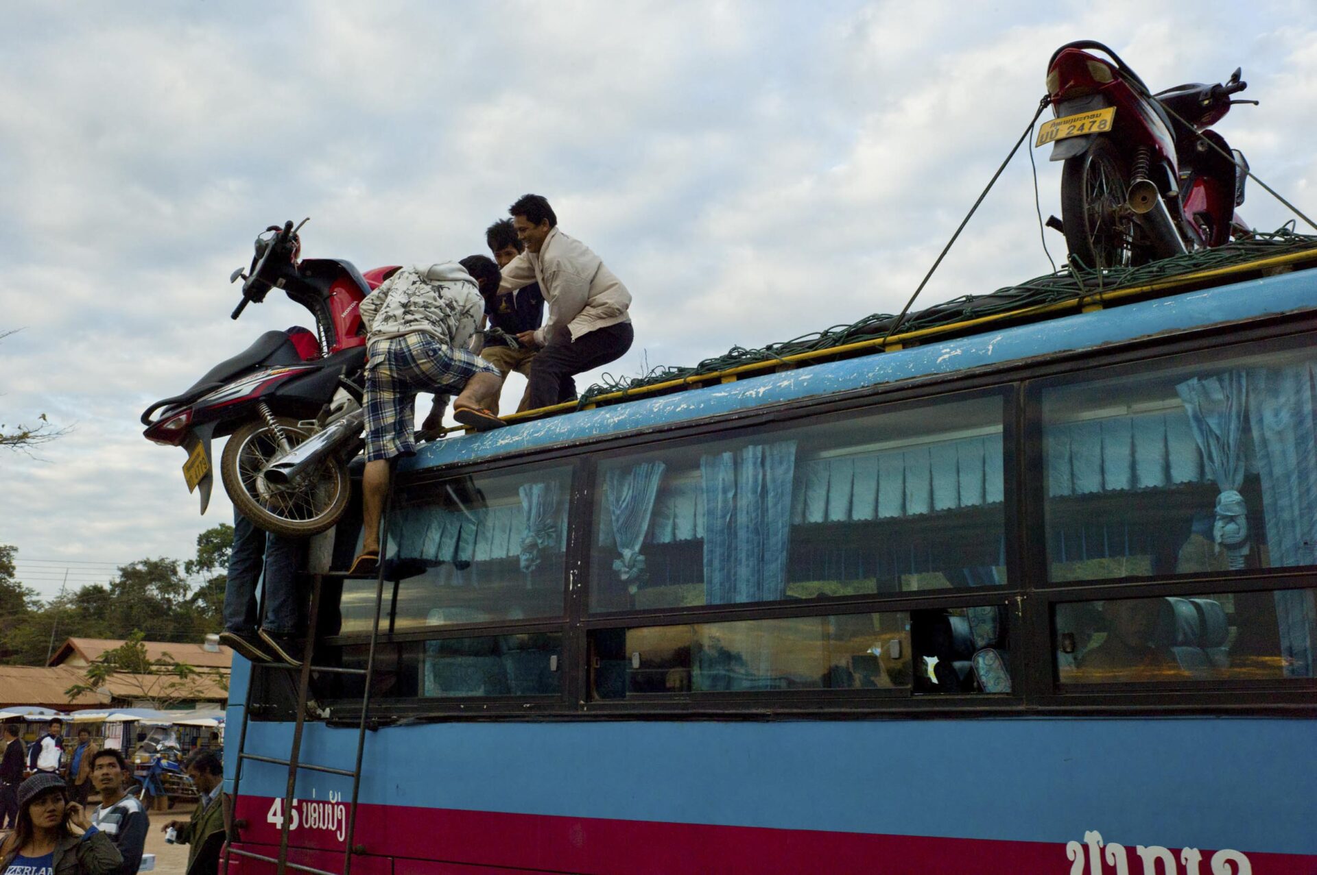 Workers load a motorbike onto the roof of a bus in Tha Khaek, 2011