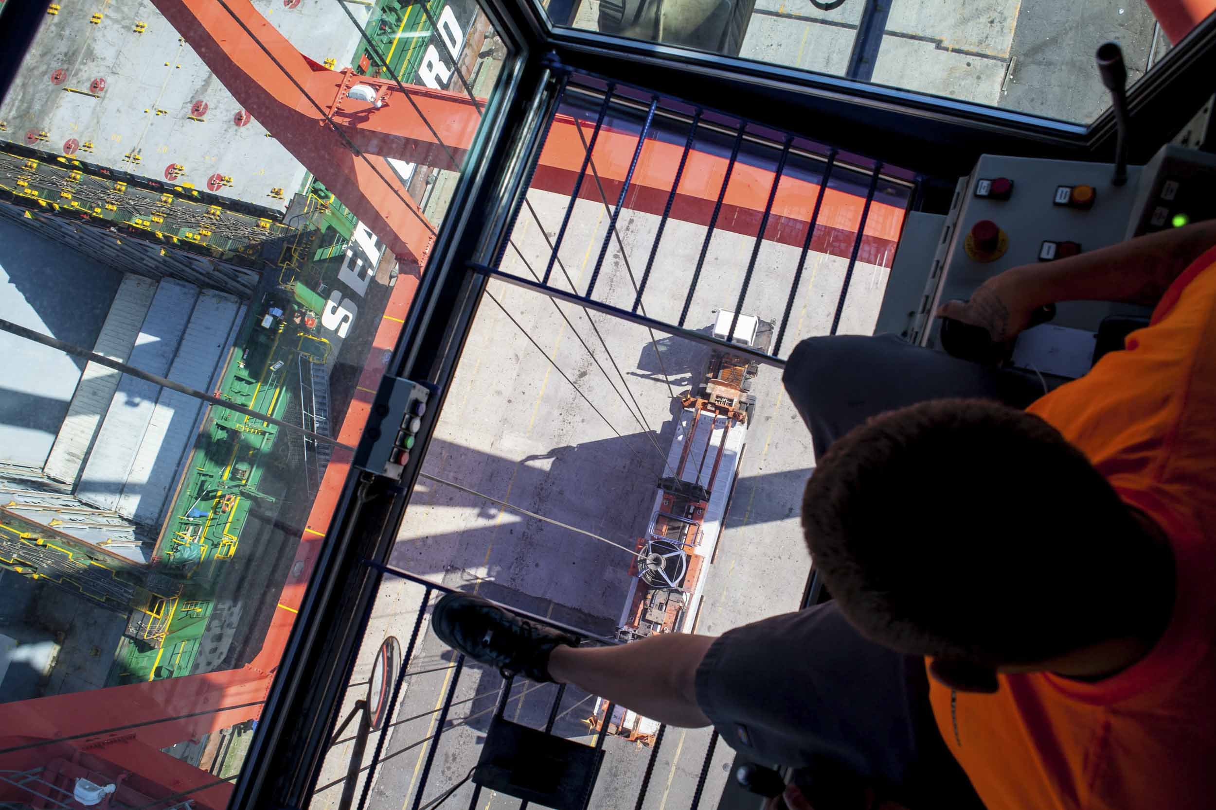 A crane operator unloads a ship and transfers the containers onto waiting trucks