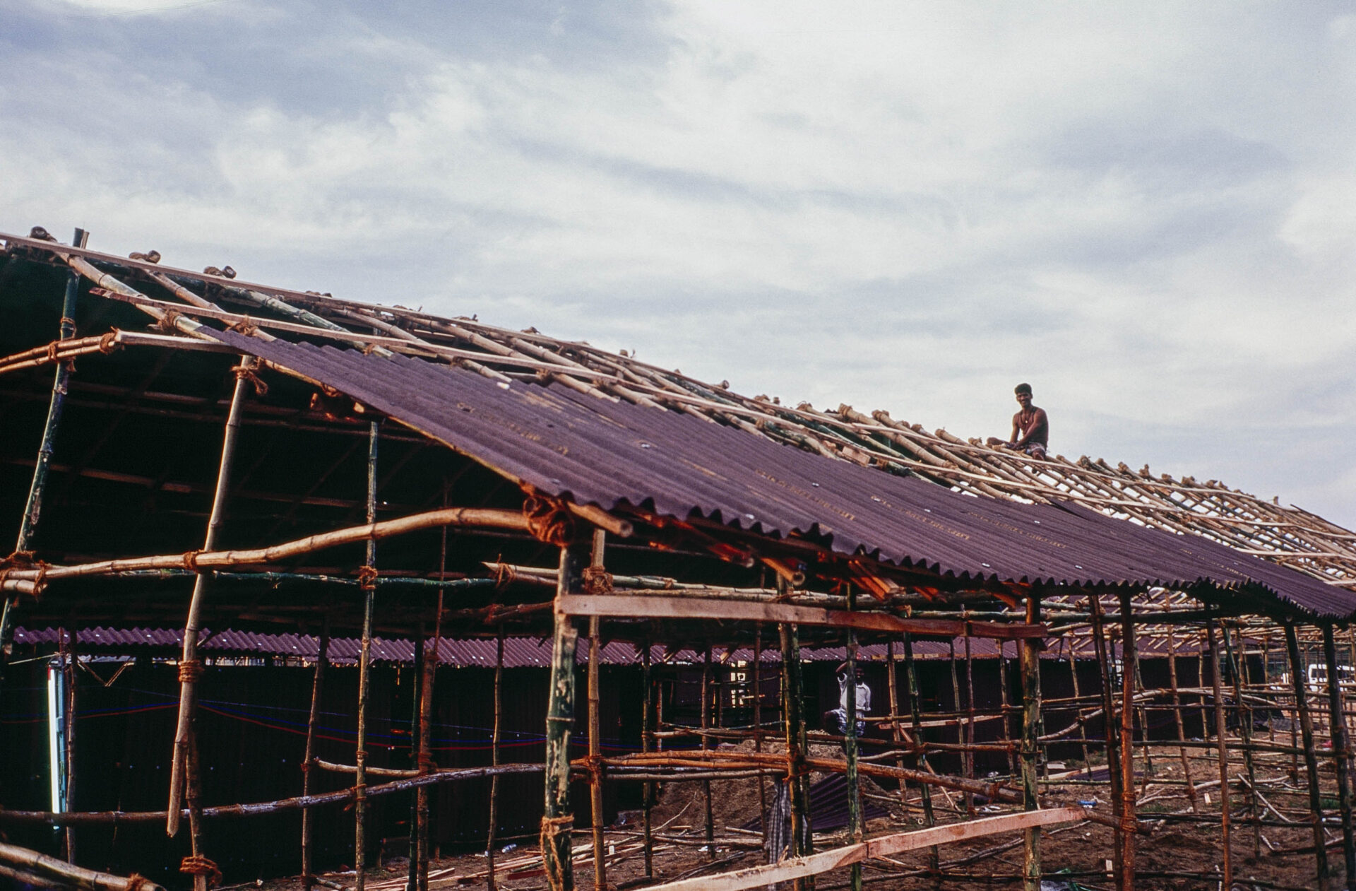 A construction worker installs corrugated tar paper roofs on shelters for tsunami survivors. Nagapattinam, India, 2005